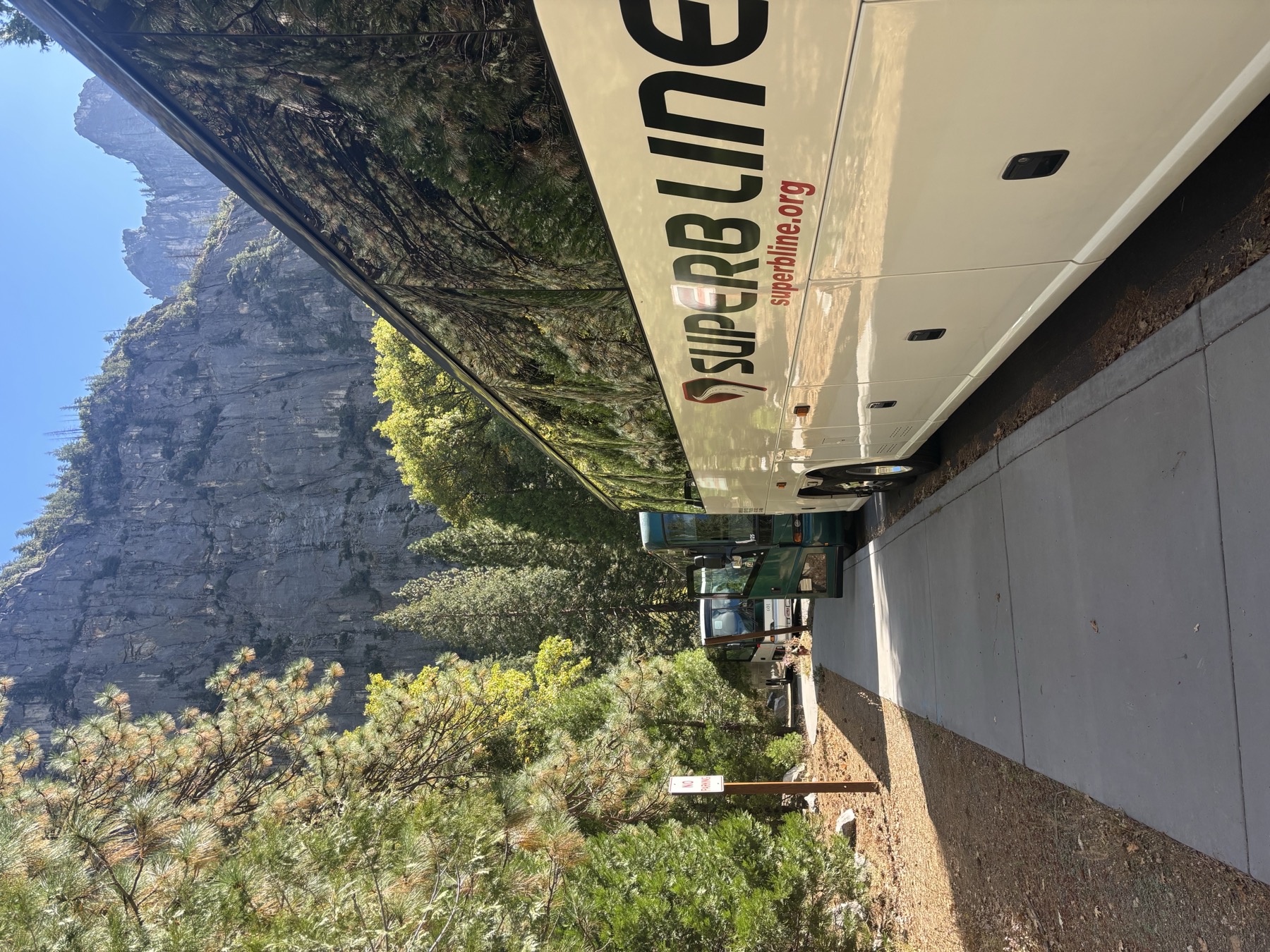 Superb Line full-size charter bus on a mountain trip, granite cliffs reflected in the windows
