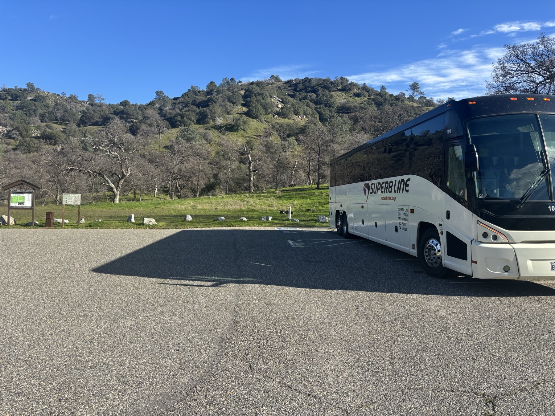 Superb Line full-size charter bus in a park-and-ride lot with oak-covered hills